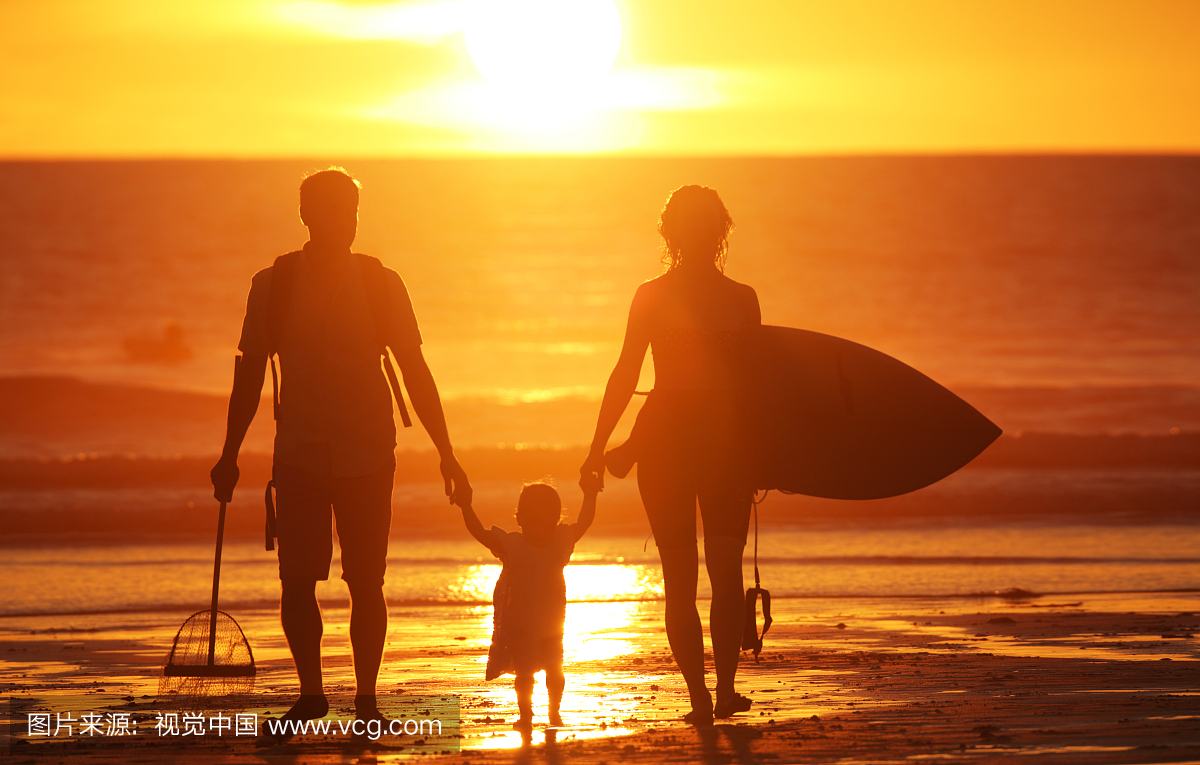 在沙滩上的家庭在日落时与冲浪板和网