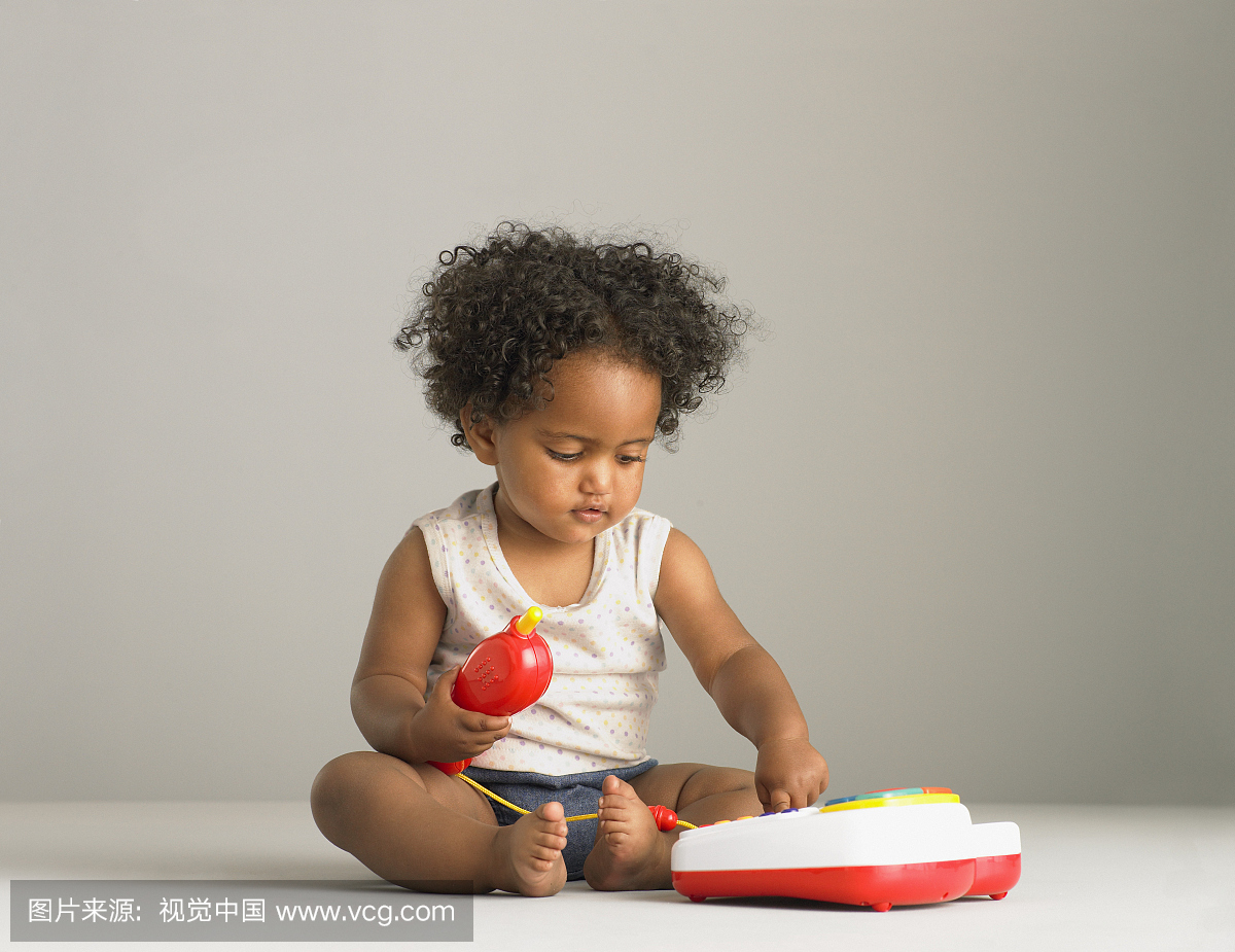 坐在玩玩具电话的地板上的女婴(14-16个月)