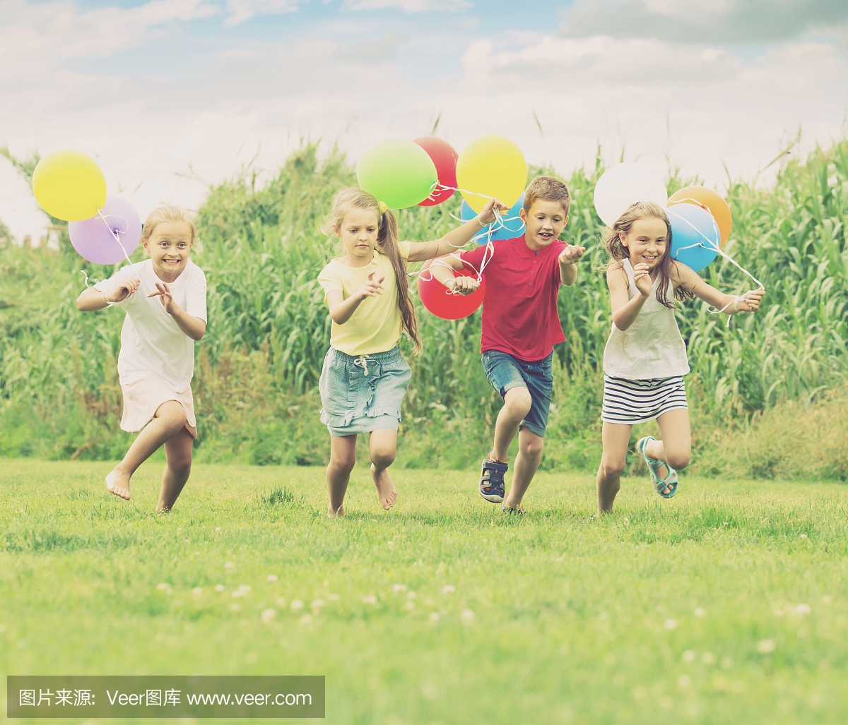 四个笑的孩子跑在绿色的草地上