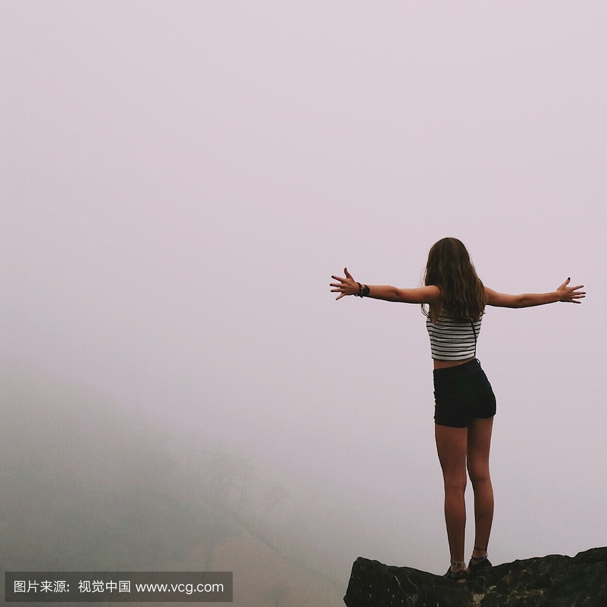 在雾天气中站在悬崖上的年轻女子的后视图