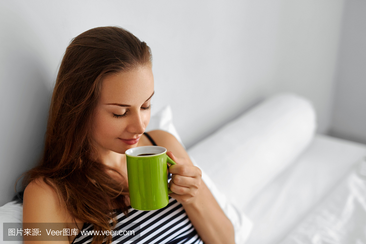 喝早晨咖啡女人喝酒在床上。健康的生活方式