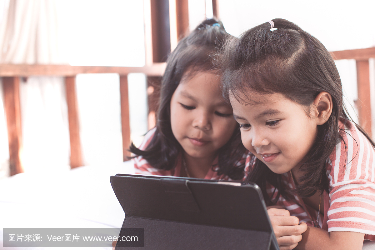 两个可爱的亚洲儿童女孩开心玩数字平板电脑游
