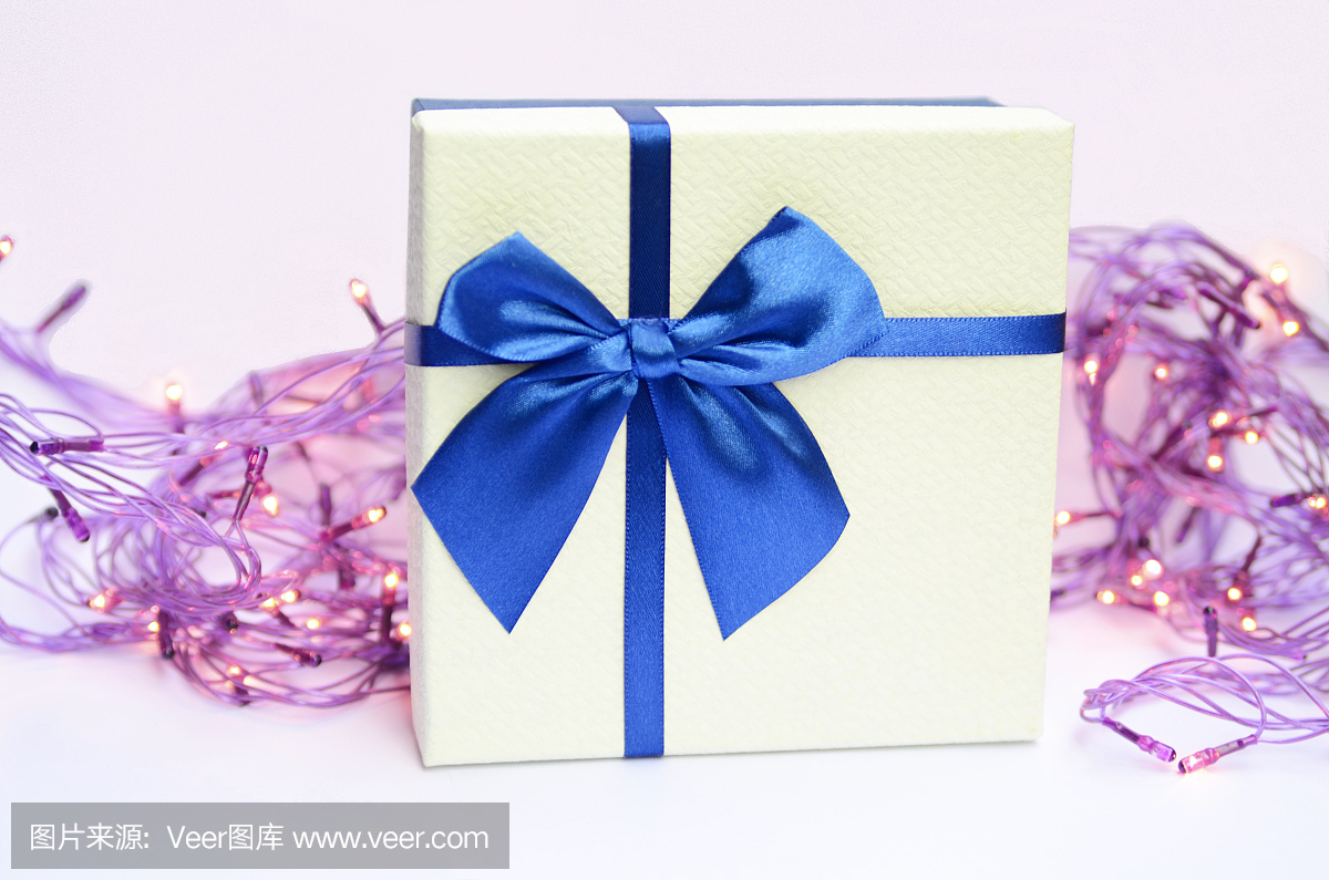 礼品盒与蓝丝带和圣诞灯在白色背景上发光。