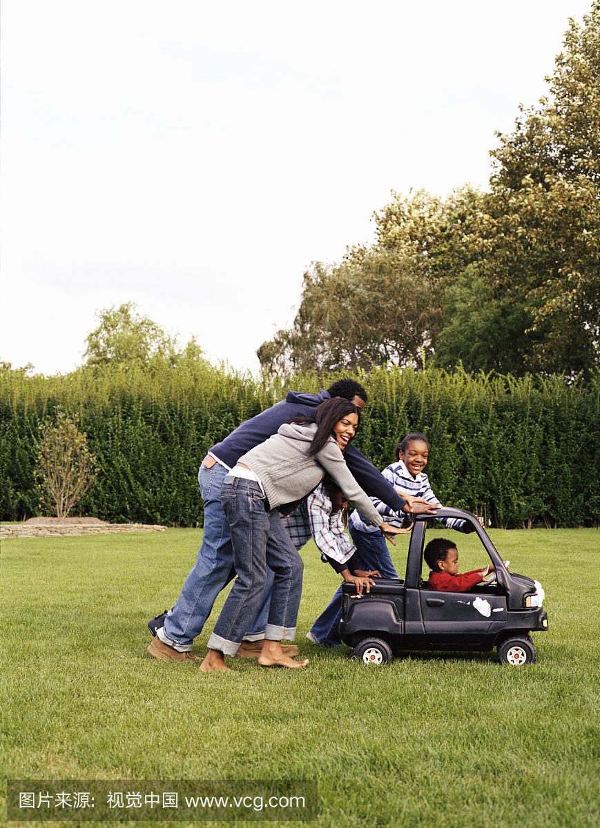 家庭推动男孩(2-4)在玩具车横过草坪