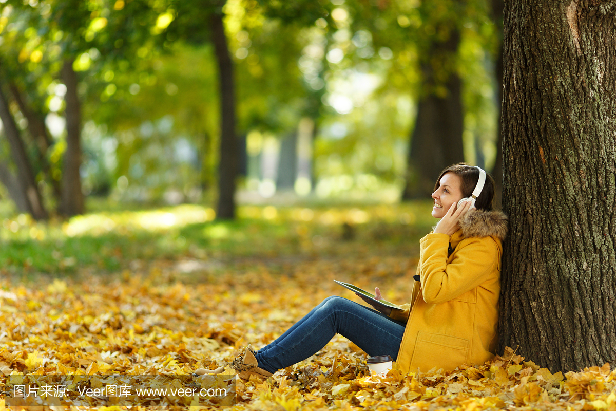 一个女人穿着黄色的外套和牛仔裤,坐在一起喝