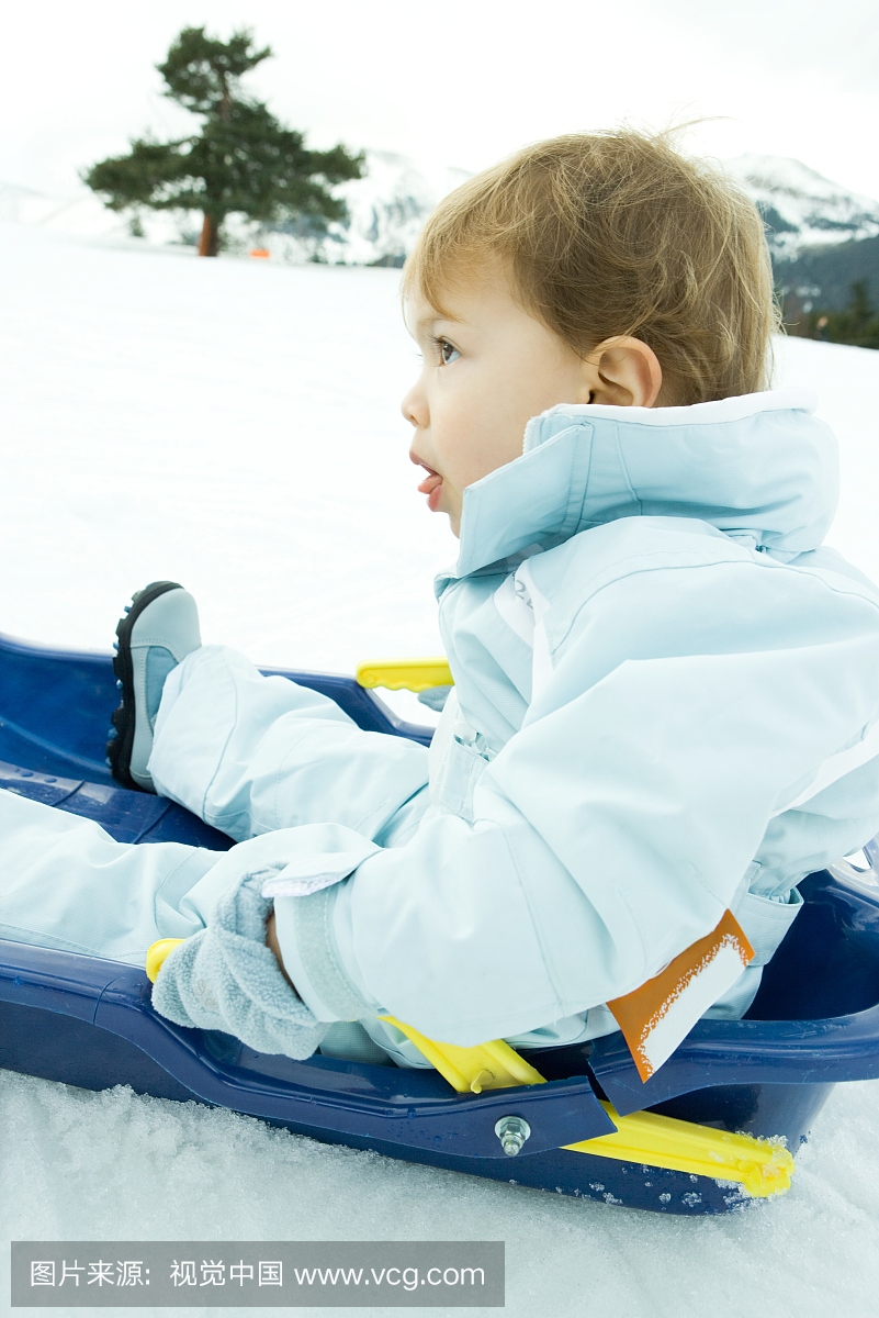 小男孩坐在雪橇上,抬起头,侧视图