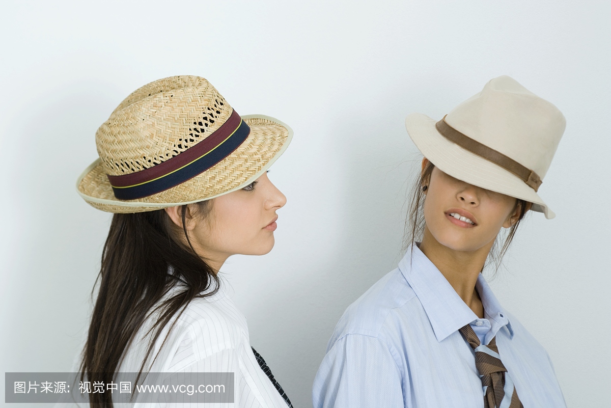 两个年轻的女性朋友穿着帽子和领带,看着对方