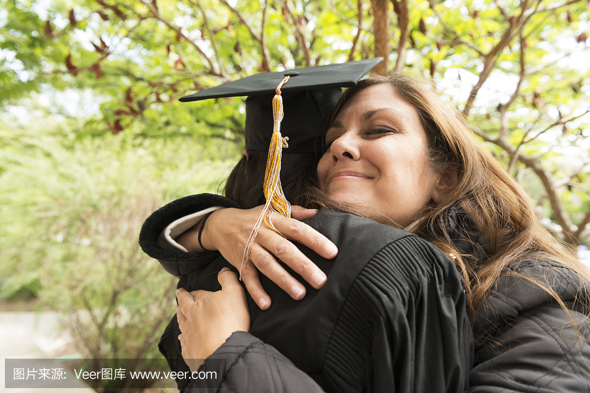 骄傲的西班牙美国母亲微笑拥抱女儿毕业学院美