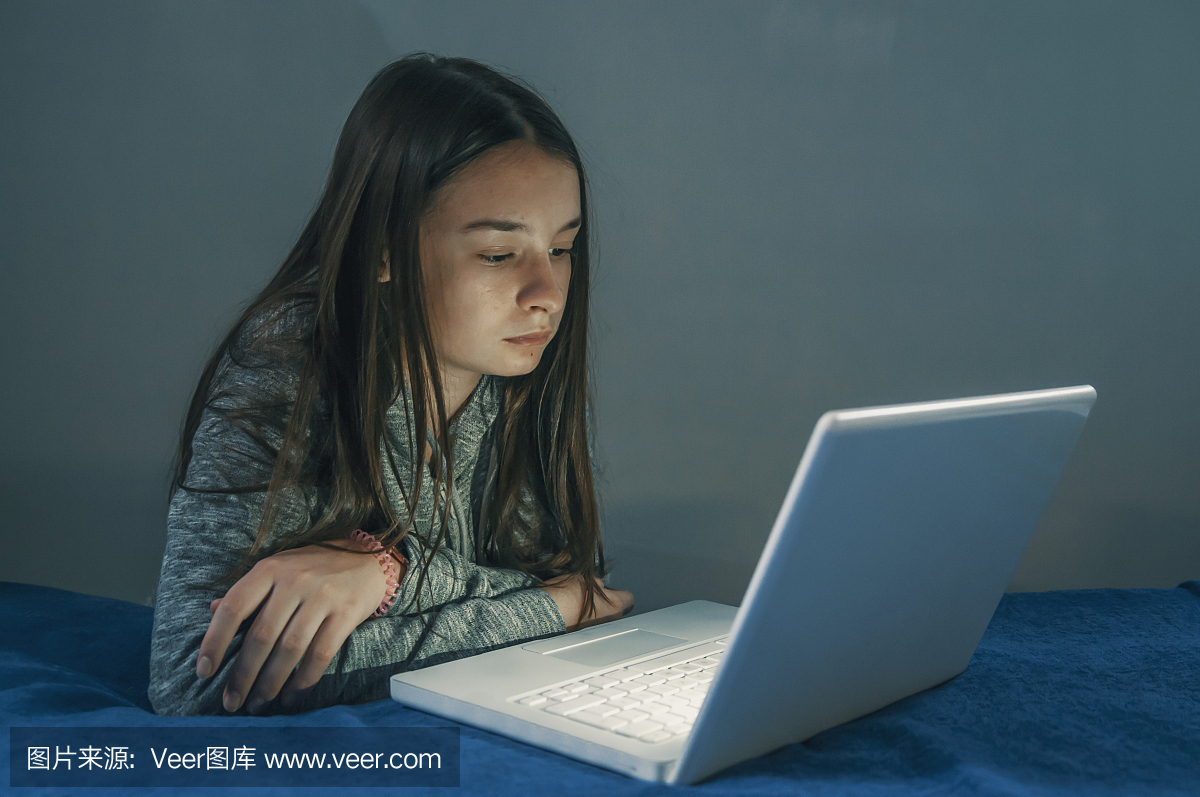 使用膝上型计算机的十几岁的女孩在卧室做家庭