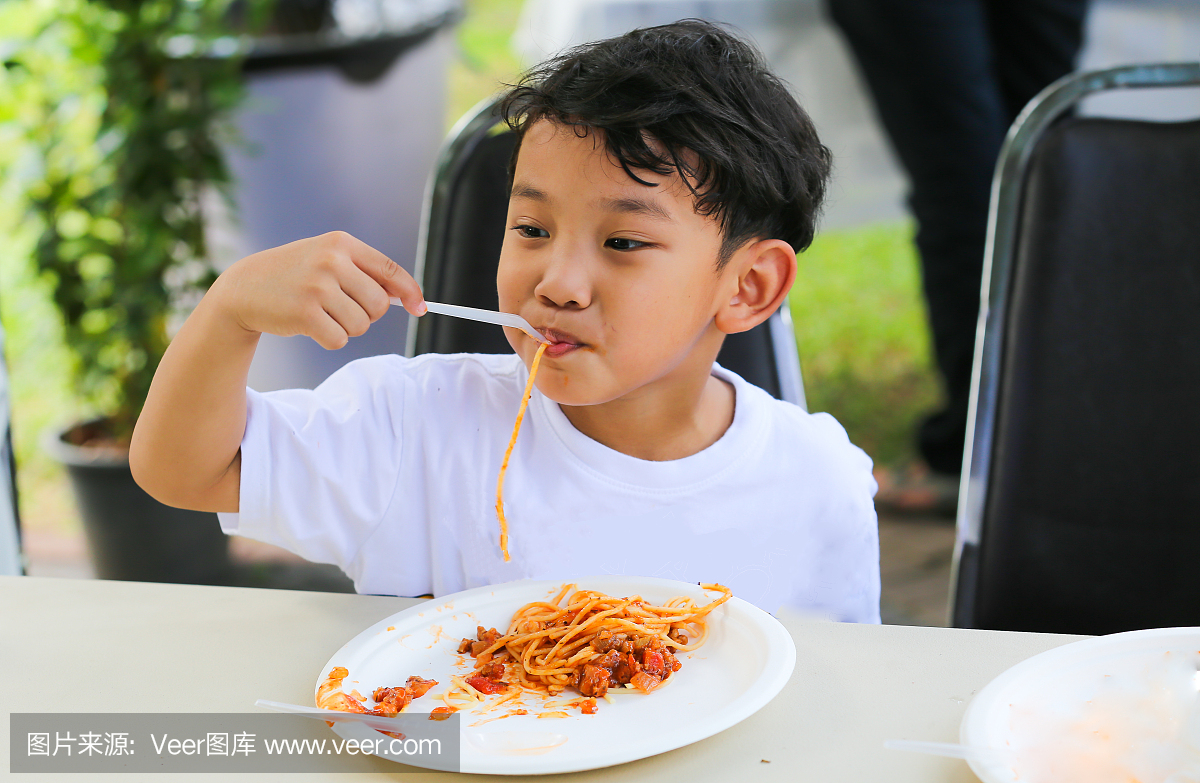 亚洲小男孩吃番茄酱意大利面吃午饭。