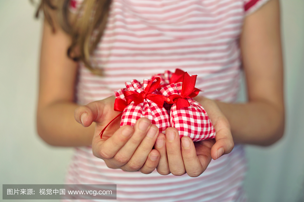关闭一个女孩拿着小礼物袋与红色领带的手。