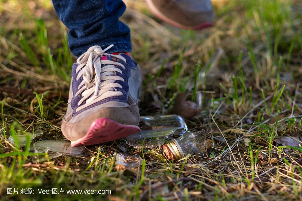 女人在运动鞋的草地上。踩在碎玻璃碎片上的危