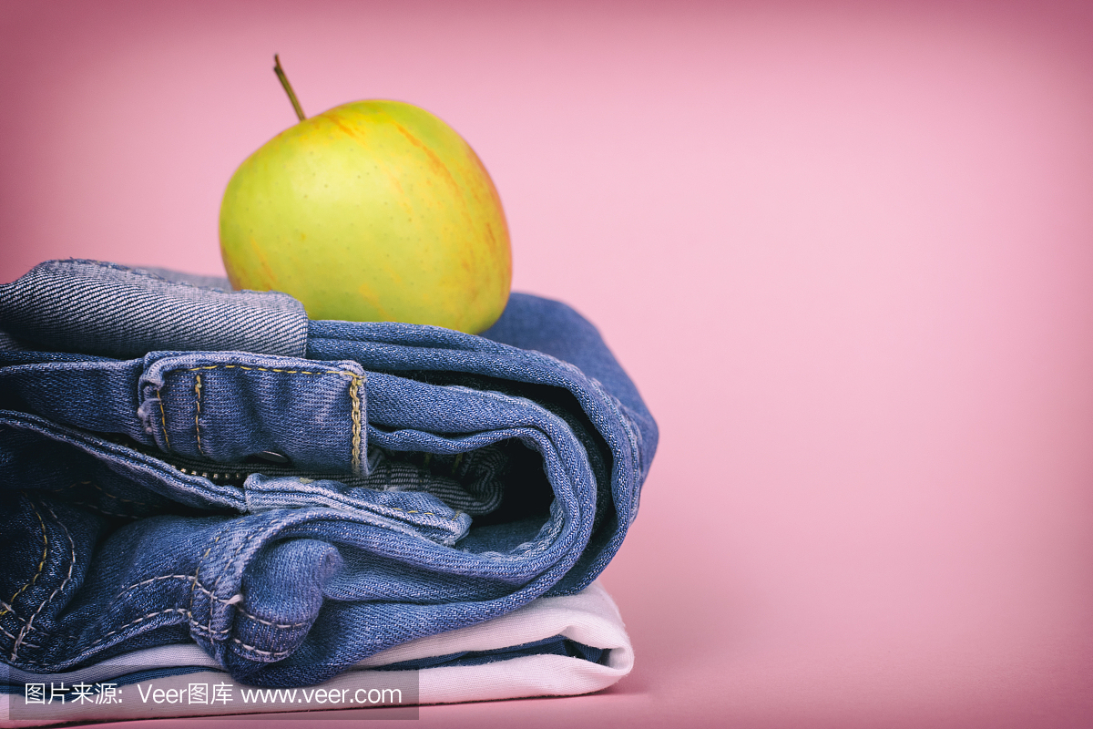 女性的牛仔裤叠成一堆,并在苹果的顶部,彩色背