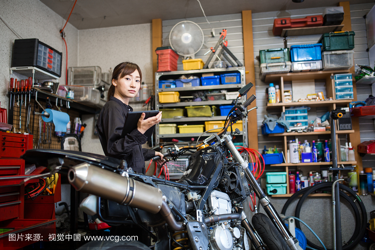 年轻的女机械师修理摩托车在她的小商业车库使