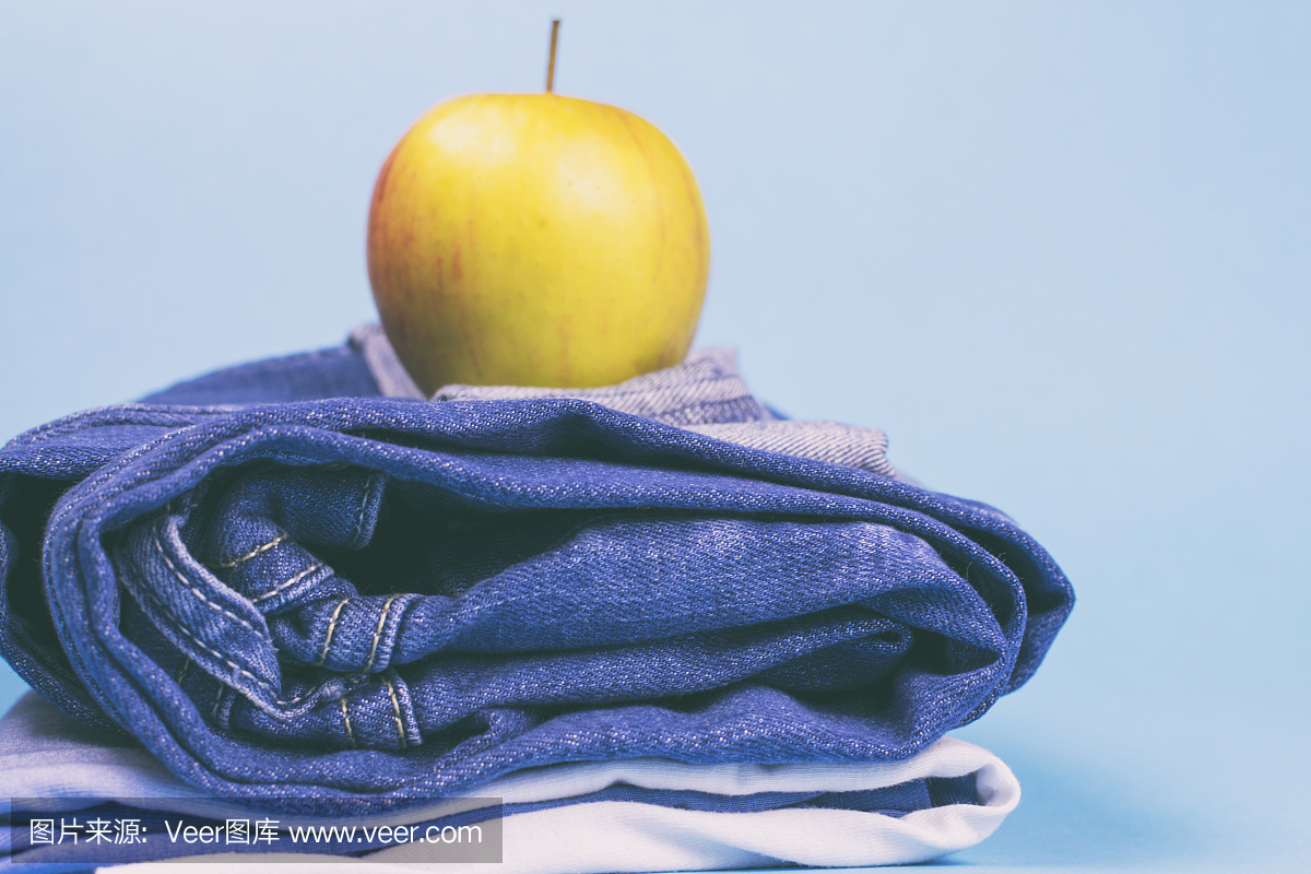 女性的牛仔裤叠成一堆,并在苹果的顶部,彩色背