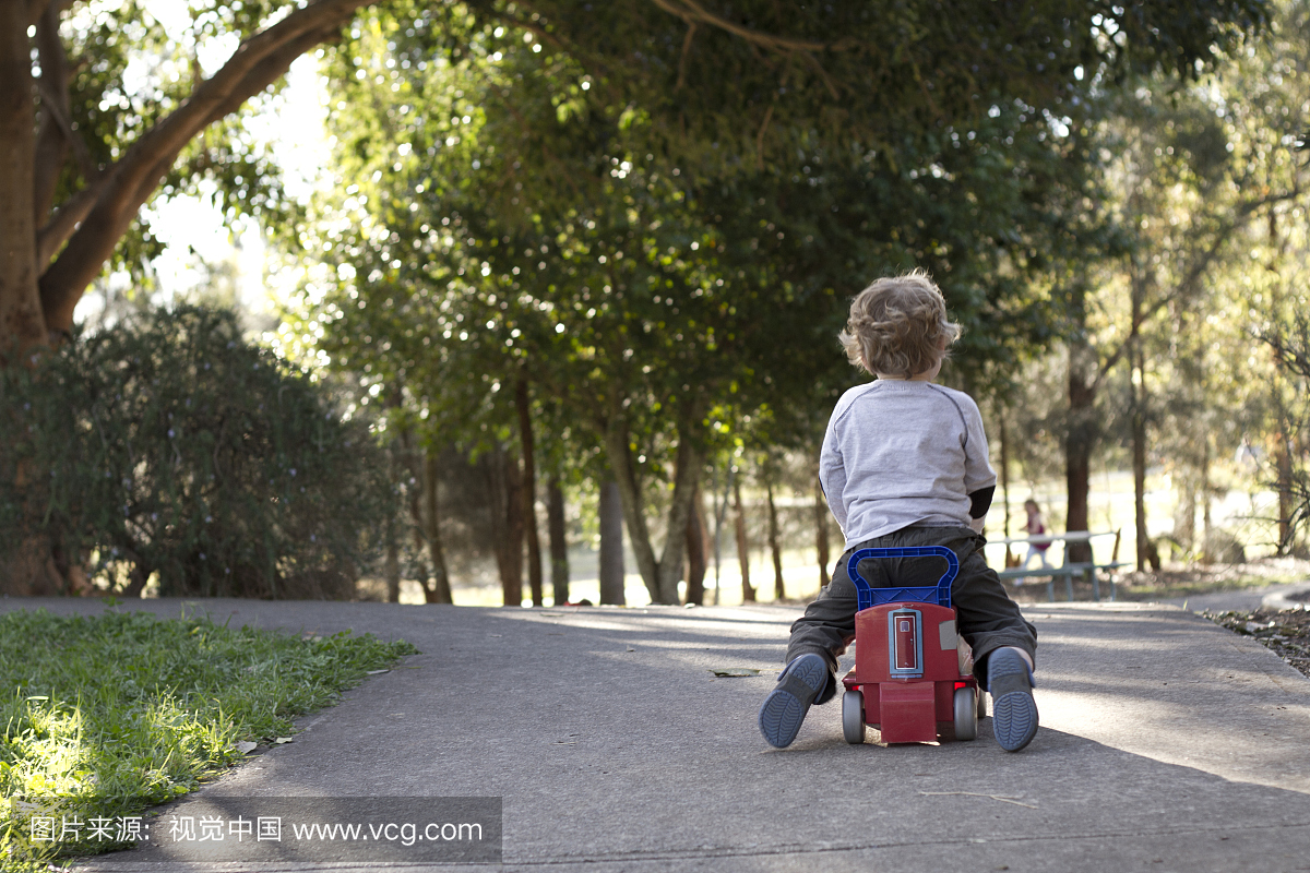 2岁的男孩骑着一辆玩具车穿过树木