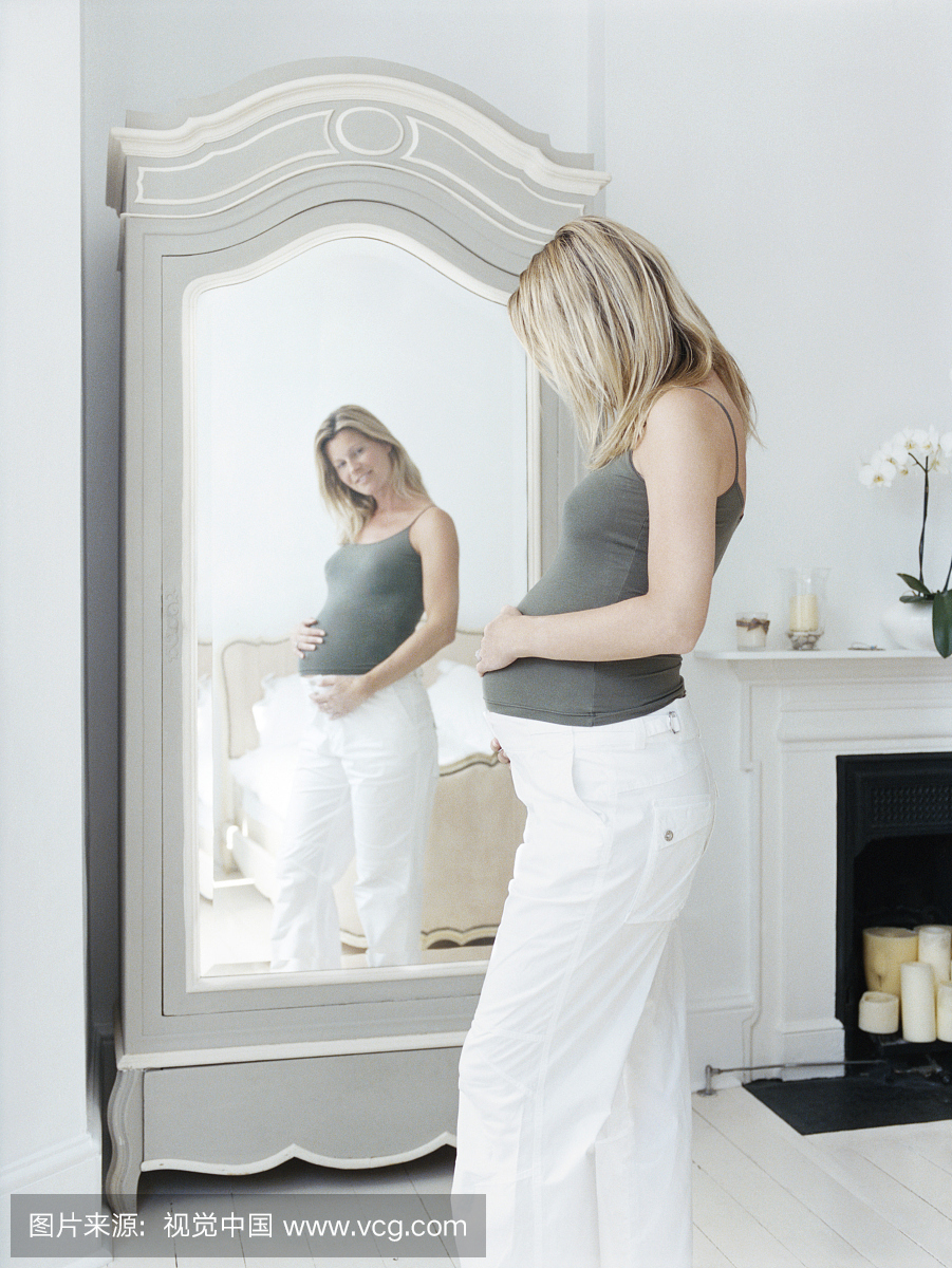 怀孕的女人看着她在镜子里的反思
