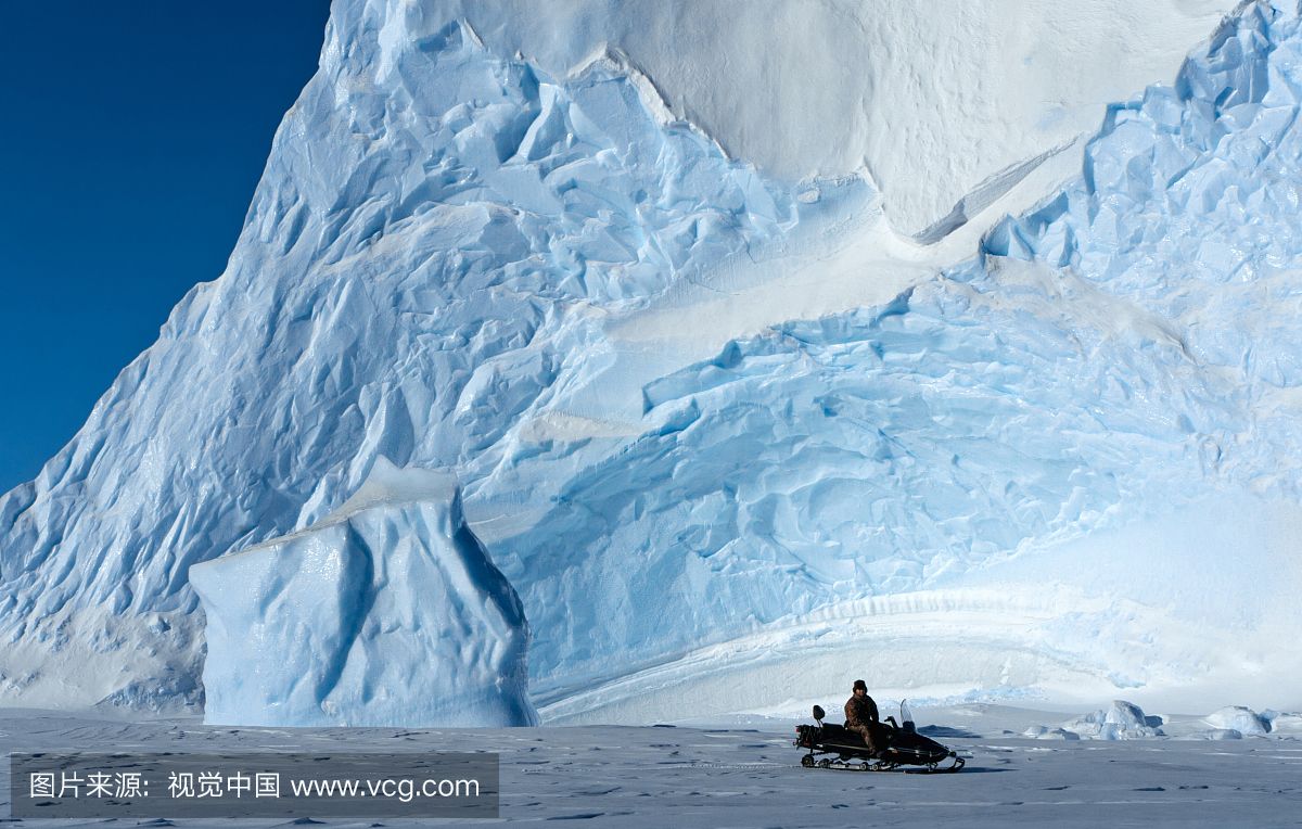 男子坐在大冰山前面的雪地摩托车上