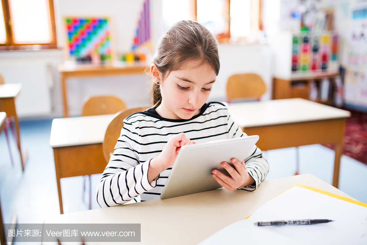 一个小女孩在学校的桌子上学习平板电脑。