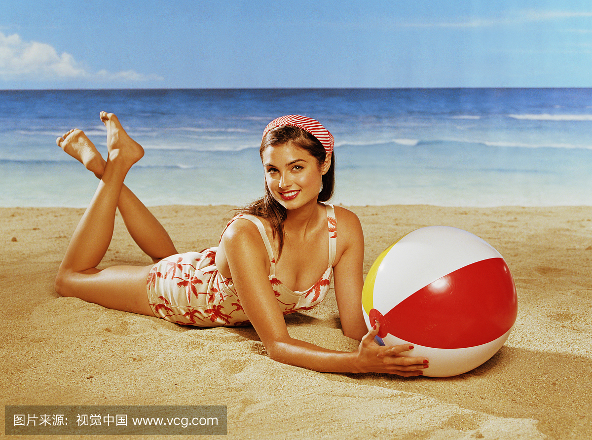 泳装的年轻女子躺在沙滩上,抱着沙滩球